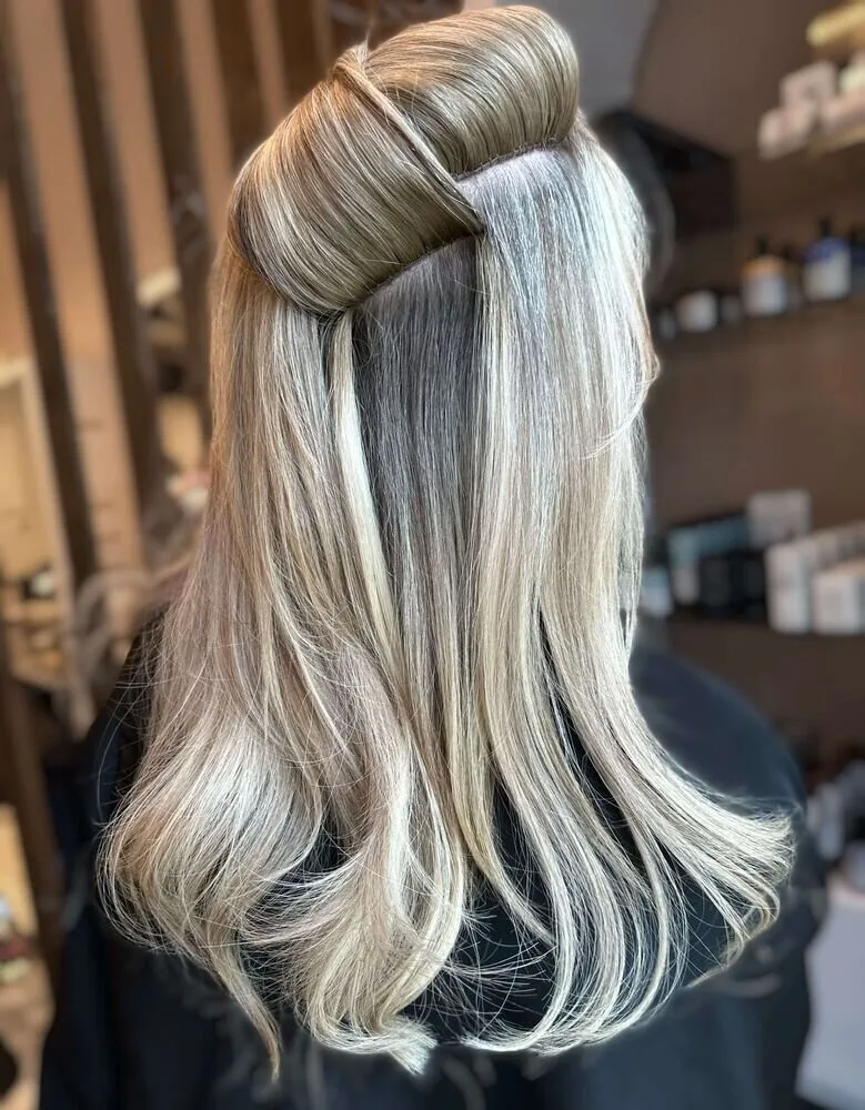 Hair sectioned and clipped up to reveal a hand-tied extension weft row installed close to the scalp, photographed from behind in a salon